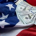 Gridlock Danger: Troops’ Paychecks in Jeopardy?! Stack of hundred dollar bills on an American flag