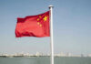 Chinese flag waving over cityscape and water.