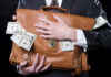 Person holding briefcase with money protruding from it.