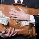 Person holding briefcase with money protruding from it.