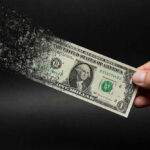 Dollar bill disintegrating while held by hand.