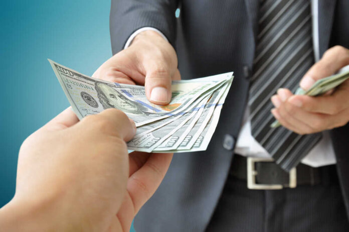 shutterstock_209123032.jpg A person handing over a stack of cash to another individual in a suit