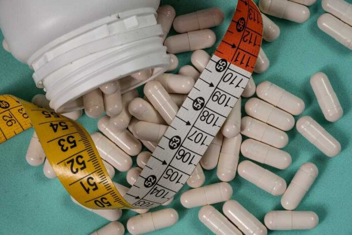 shutterstock_2600295527.jpg White capsules scattered around a measuring tape and a bottle