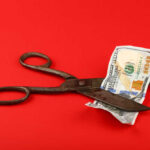 Millions Face Wage Cuts: Trump Policy Now Activated Scissors cutting a hundred dollar bill on a red background