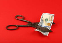 Scissors cutting a hundred dollar bill on a red background