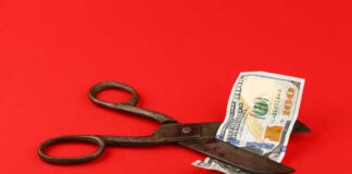 Scissors cutting a hundred dollar bill on a red background