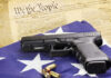 A handgun resting on an American flag with bullets and a historical document in the background