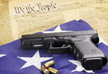 A handgun resting on an American flag with bullets and a historical document in the background