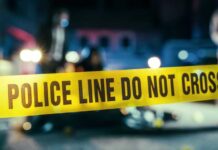 Police line caution tape at a crime scene with blurred figures in the background