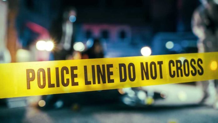 shutterstock_2230645949.jpg Police line caution tape at a crime scene with blurred figures in the background