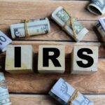IRS Workforce SLASHED: Refund Chaos Looms Wooden blocks spelling IRS surrounded by rolled currency notes