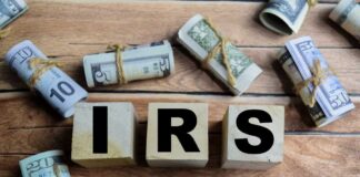 Wooden blocks spelling IRS surrounded by rolled currency notes