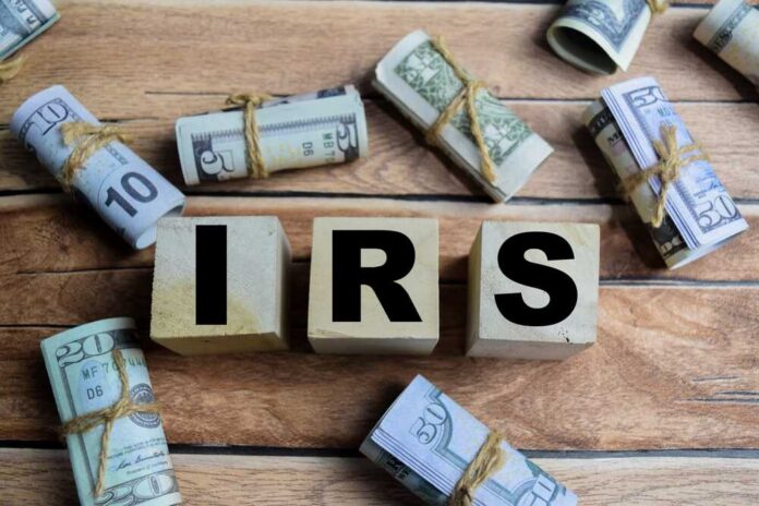 shutterstock_2606280847.jpg Wooden blocks spelling IRS surrounded by rolled currency notes