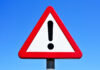 A triangular warning sign with an exclamation mark against a blue sky
