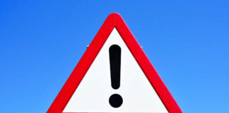 A triangular warning sign with an exclamation mark against a blue sky