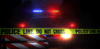 Police car with flashing lights behind caution tape.