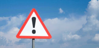 Triangle warning sign with exclamation mark against sky.