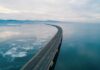 Aerial view of a curved bridge over a calm, icy body of water