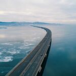 Aerial view of a curved bridge over a calm, icy body of water