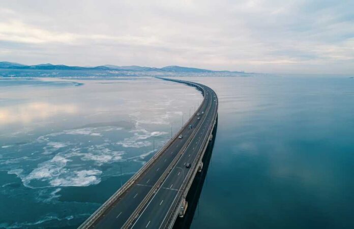 Aerial view of a curved bridge over a calm, icy body of water