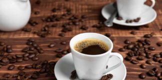 A white coffee cup filled with coffee on a wooden table surrounded by coffee beans