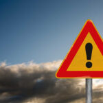 Regime CRUSHED — But Election Mystery Deepens A triangular warning sign with an exclamation mark against a cloudy sky