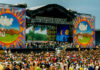 LEGENDARY Woodstock Icon DIES — Untold Military Past A large crowd at an outdoor music festival with a vibrant stage