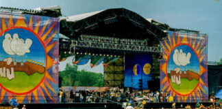 A large crowd at an outdoor music festival with a vibrant stage