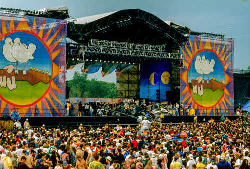 A large crowd at an outdoor music festival with a vibrant stage