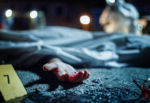 Crime scene with covered body and hand exposed.