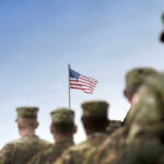 Soldiers in uniform with American flag in background.