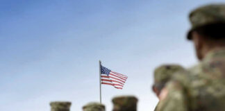 Soldiers in uniform with American flag in background.