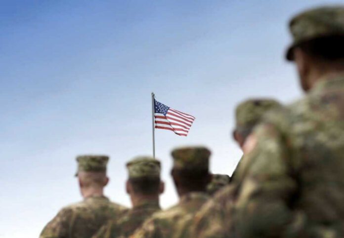Soldiers in uniform with American flag in background.