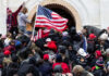 Crowd storming a building, waving an American flag.