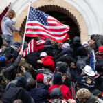 Crowd storming a building, waving an American flag.