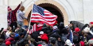 Crowd storming a building, waving an American flag.