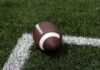 A brown football resting on green artificial turf near a white line