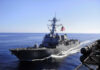 US Bombs Iran Amid Ceasefire Peace Talk Warship with American flag sailing in the ocean.