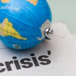 Ebola Crosses Borders: Global Crisis Looms? A small globe resting on a newspaper with the word 'crisis'