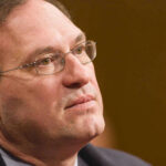 Close-up of a man wearing glasses, looking thoughtful.