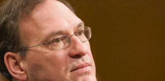 Close-up of a man wearing glasses, looking thoughtful.