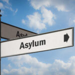 Supreme Court Shocker Reshapes Asylum Border patrol officer watches group sitting by a fence.