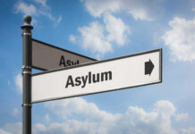 Supreme Court Shocker Reshapes Asylum Border patrol officer watches group sitting by a fence.