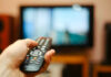 Hand holding a remote control towards a TV screen.