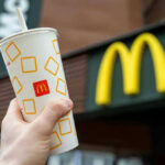 Shocking Hot Oil Attack Inside McDonald’s Hand holding McDonalds cup in front of restaurant sign.