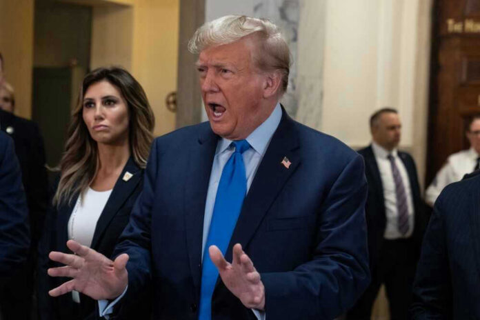 Donald Trump speaking with hands raised in a hallway